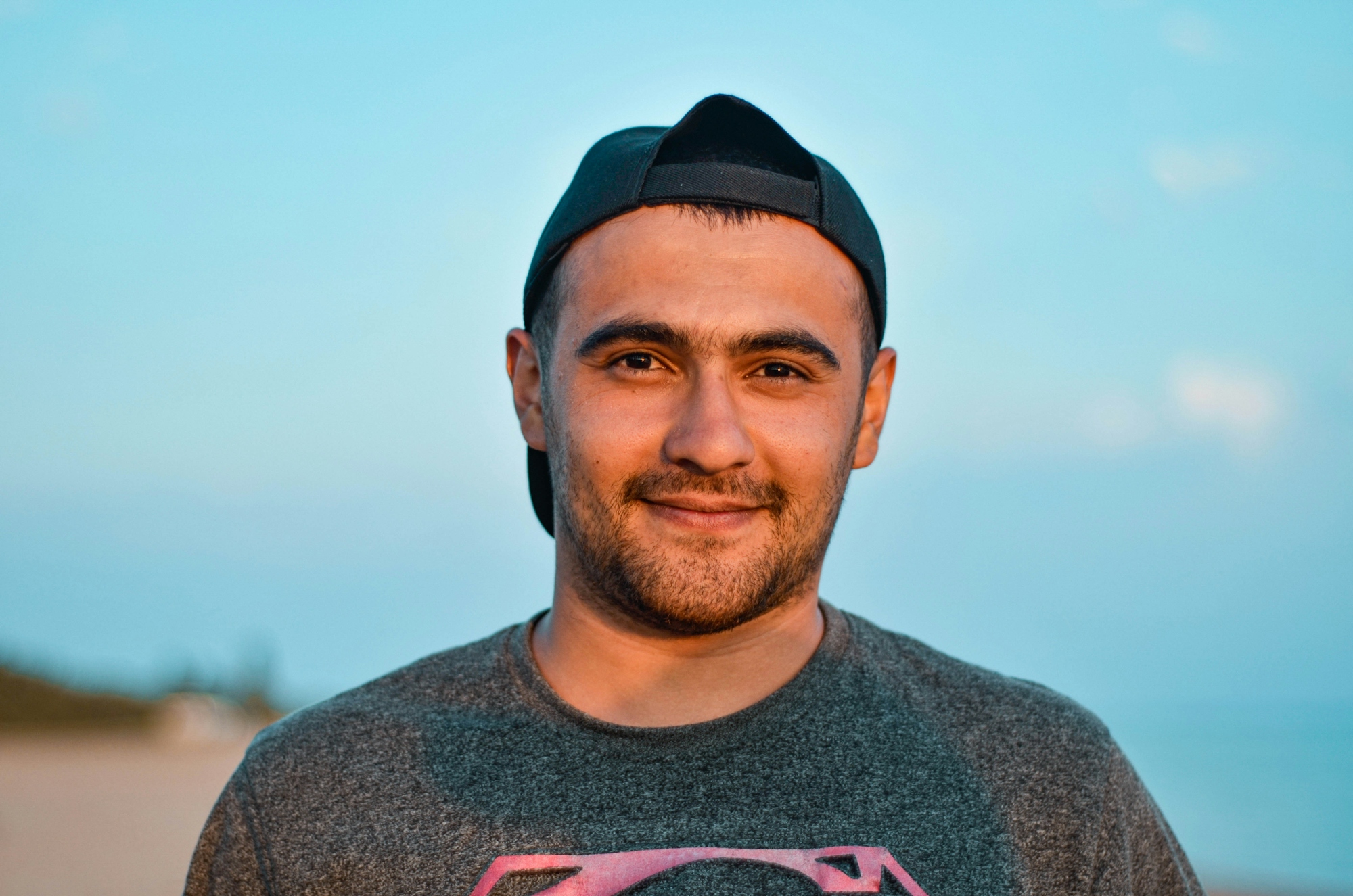 A man wearing a black baseball cap and grey t-shirt against a blue sky